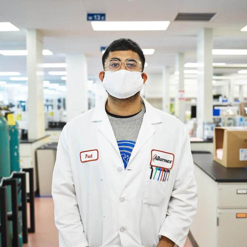 Man standing in lab coat with mask on in laboratory area at Alkermes.