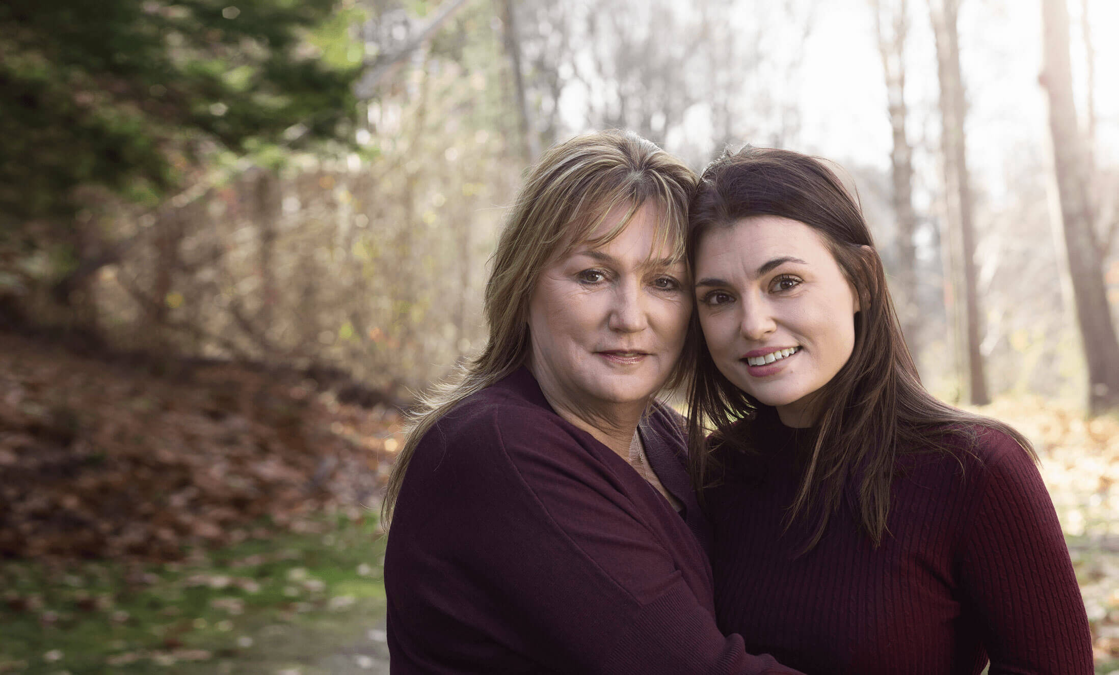 Mother hugging her smiling daughter with trees in background