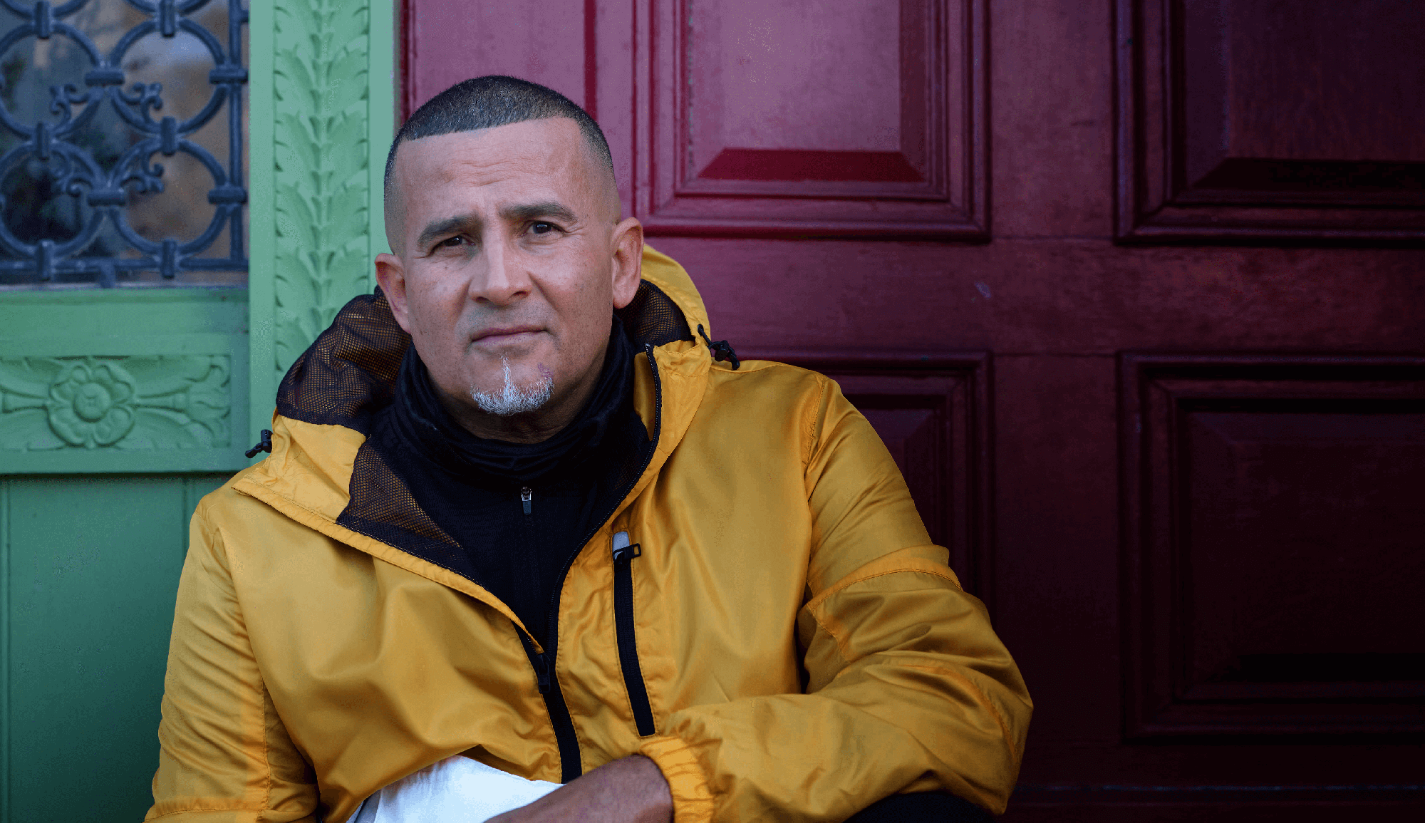 Man in yellow jacket sitting on outdoor steps of building with red door