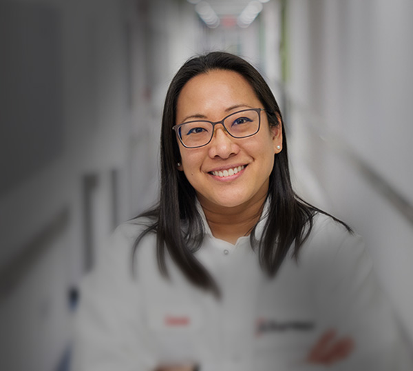 woman wearing safety glasses and a labcoat smiling while working in lab
