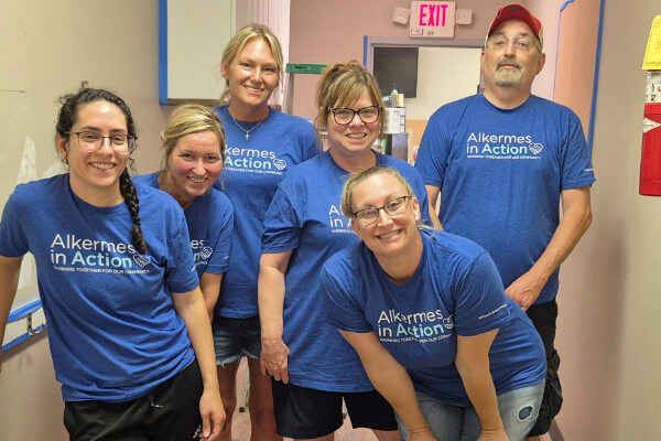 six employees standing in a hallway wearing Alkermes in Action t-shirts