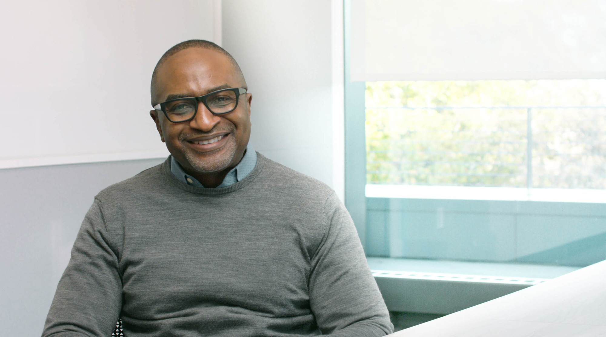 Smiling man with glasses sitting at table in Alkermes conference room with window in background 